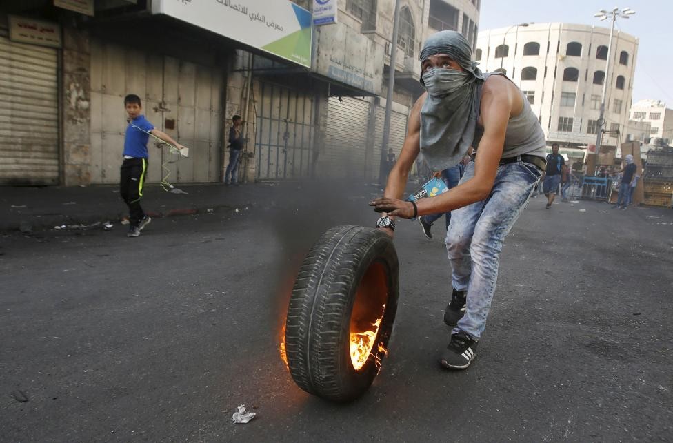 Các cuộc  đụng độ đẫm máu Palestine-Israel diễn ra trong suốt tuần qua đang có dấu hiệu leo thang. Xung đột xảy ra ở khu vực Thành cổ Jersusalem hôm 3/10 khi một binh sĩ Israel cùng một giáo sĩ Do Thái bị đâm chết. Một vài giờ sau, một thiếu niên Israel cũng bị một người Palestine đâm. Trong ảnh, một người Palestine quăng lốp xe đang cháy về phía lính Israel ở thành phố Hebron, thành phố Bờ Tây.